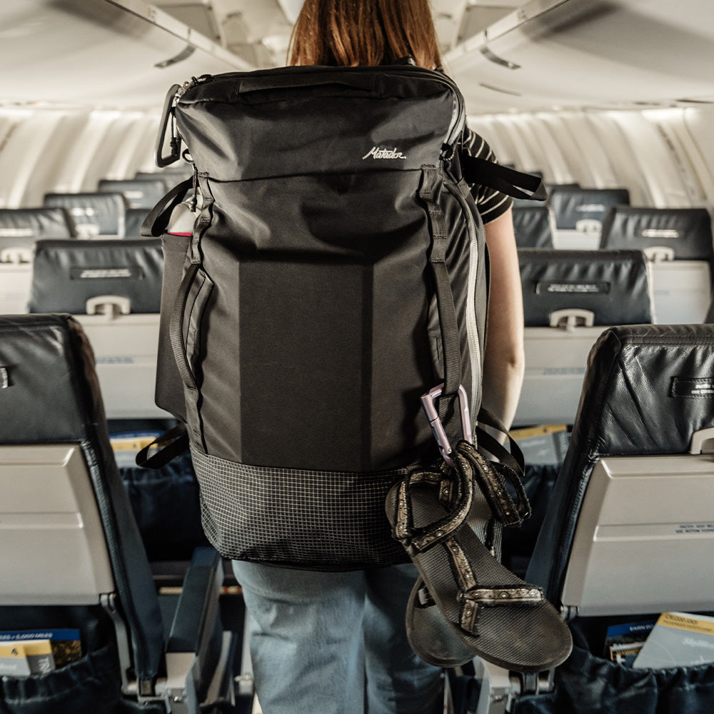 woman walking down airplane aisle with shoes handing off bag by carabiner